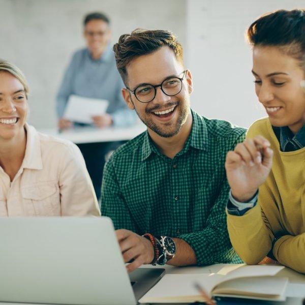 Happy student having fun while using laptop with his friends in Formas de Titulación